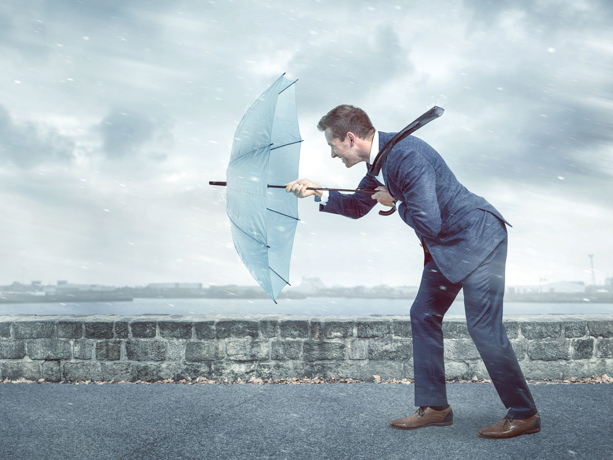 Mann stemmt sich mit Regenschirm gegen Sturm als Symbol für das Lernen von Resilienz
